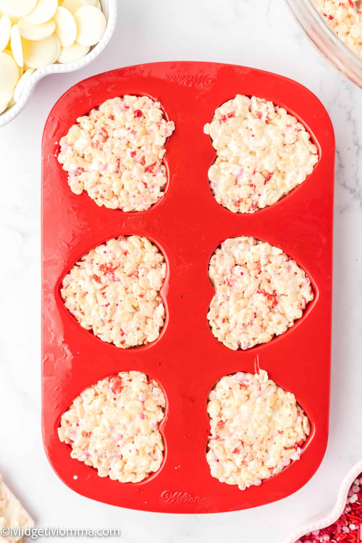 Heart-shaped molds filled with a rice crispy mixture on a red silicone tray.