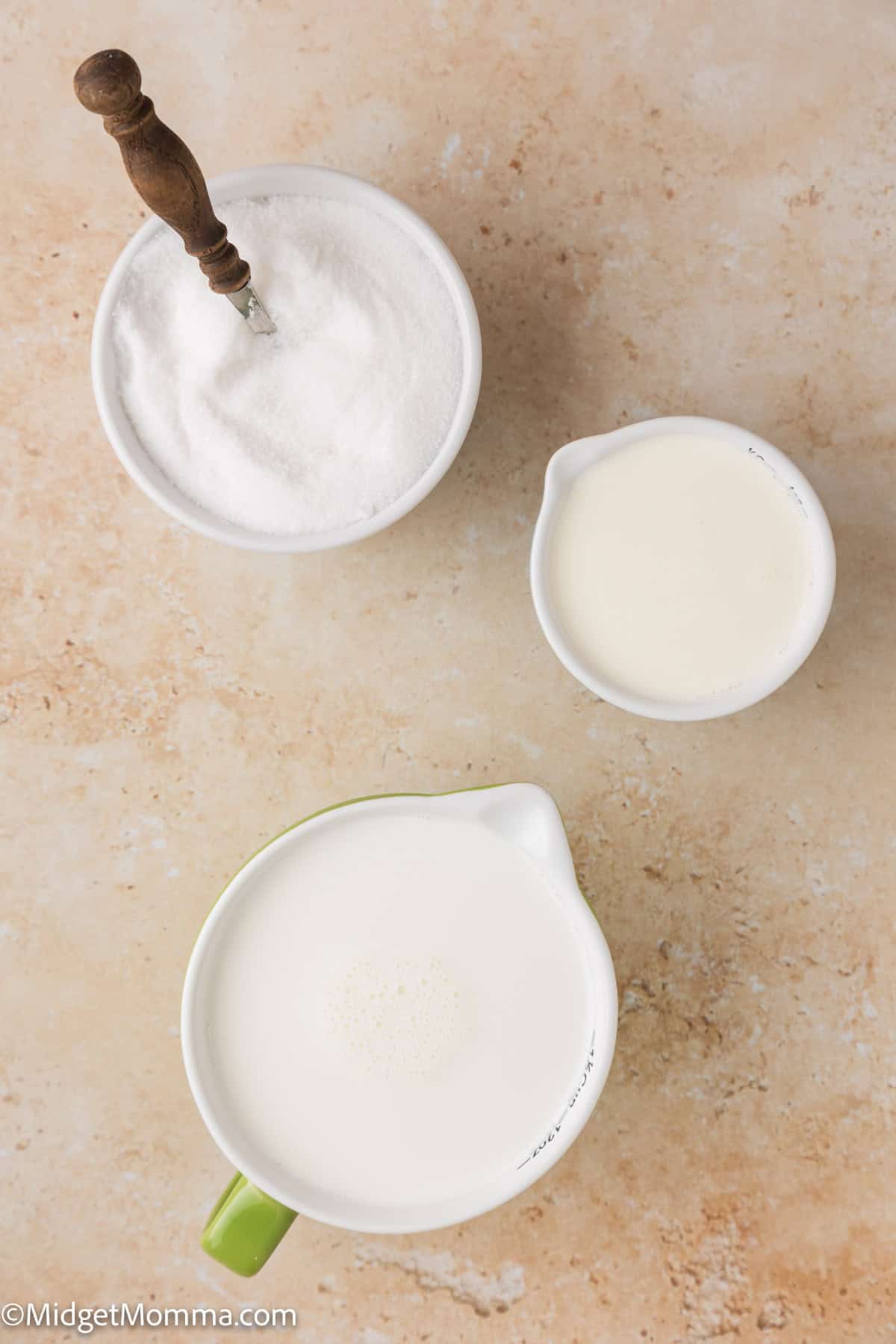 Bowls on a countertop with sugar, half and half, and heavy cream; a wooden spoon rests in the sugar.