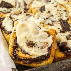 A tray of frosted cinnamon rolls with crushed cookie pieces on top.