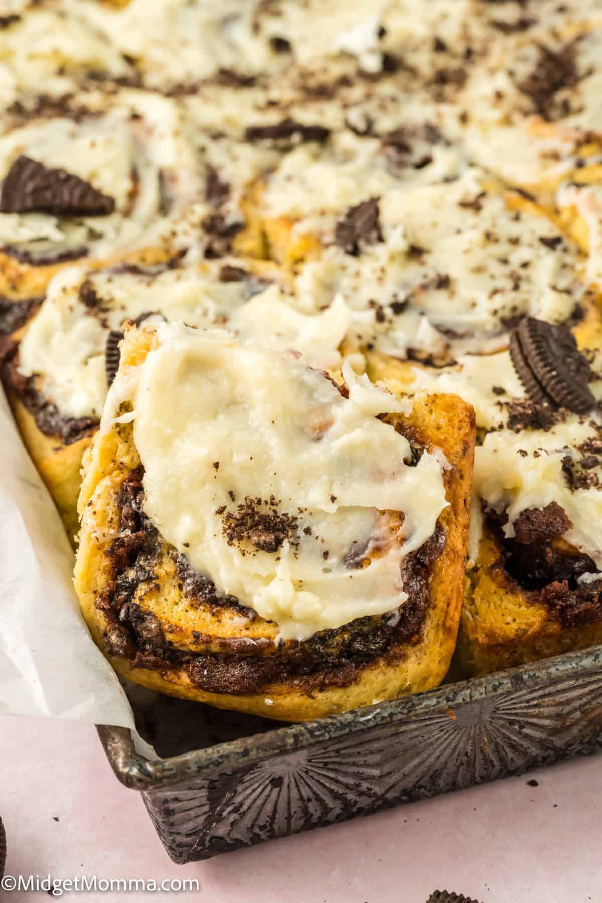 A tray of frosted cinnamon rolls with crushed cookie pieces on top.