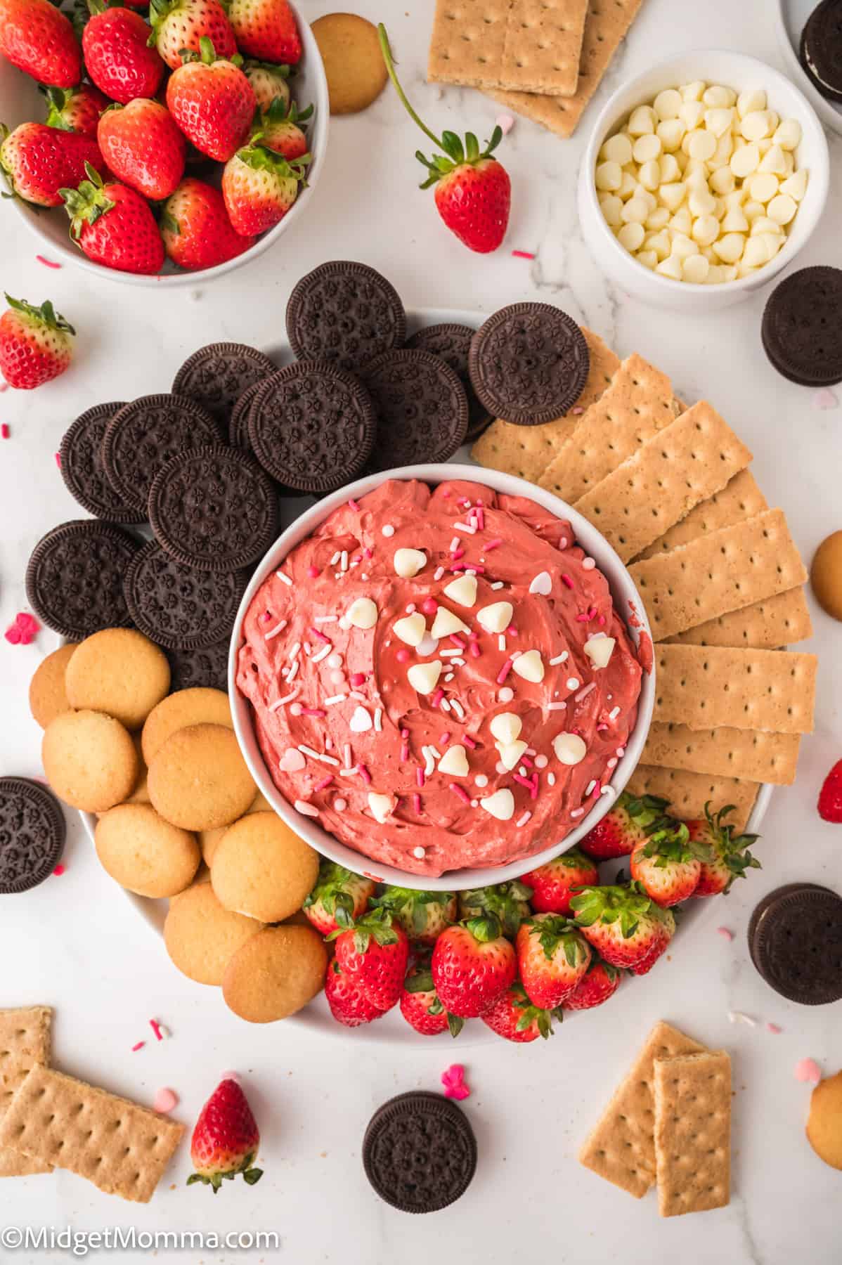 Colorful dessert platter with a bowl of red velvet dip, chocolate and vanilla cookies, graham crackers, strawberries, and white chocolate chips.