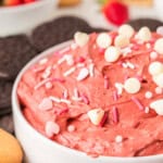 A bowl of red velvet cheesecake dessert dip topped with sprinkles, surrounded by cookies and strawberries.