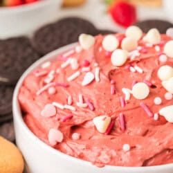 A bowl of red velvet cheesecake dessert dip topped with sprinkles, surrounded by cookies and strawberries.