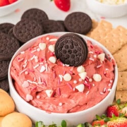 A bowl of red velvet dip topped with a chocolate cookie, surrounded by strawberries, chocolate cookies, graham crackers, and vanilla wafers.