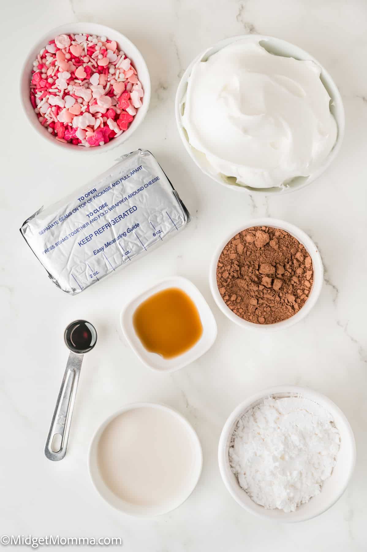 Red Velvet Cheesecake Dip ingredients. Ingredients for a dessert include whipped cream, chocolate powder, food coloring, cream cheese, vanilla extract, and a small bowl of milk on a white surface.