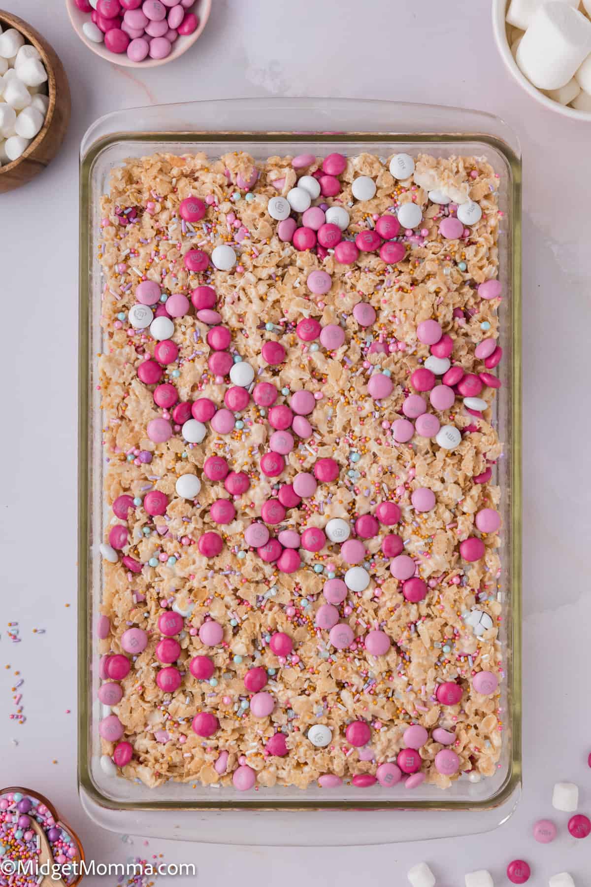 Top view of a rectangular tray filled with colorful rice cereal treats topped with pink, purple, and white candies, and sprinkles.