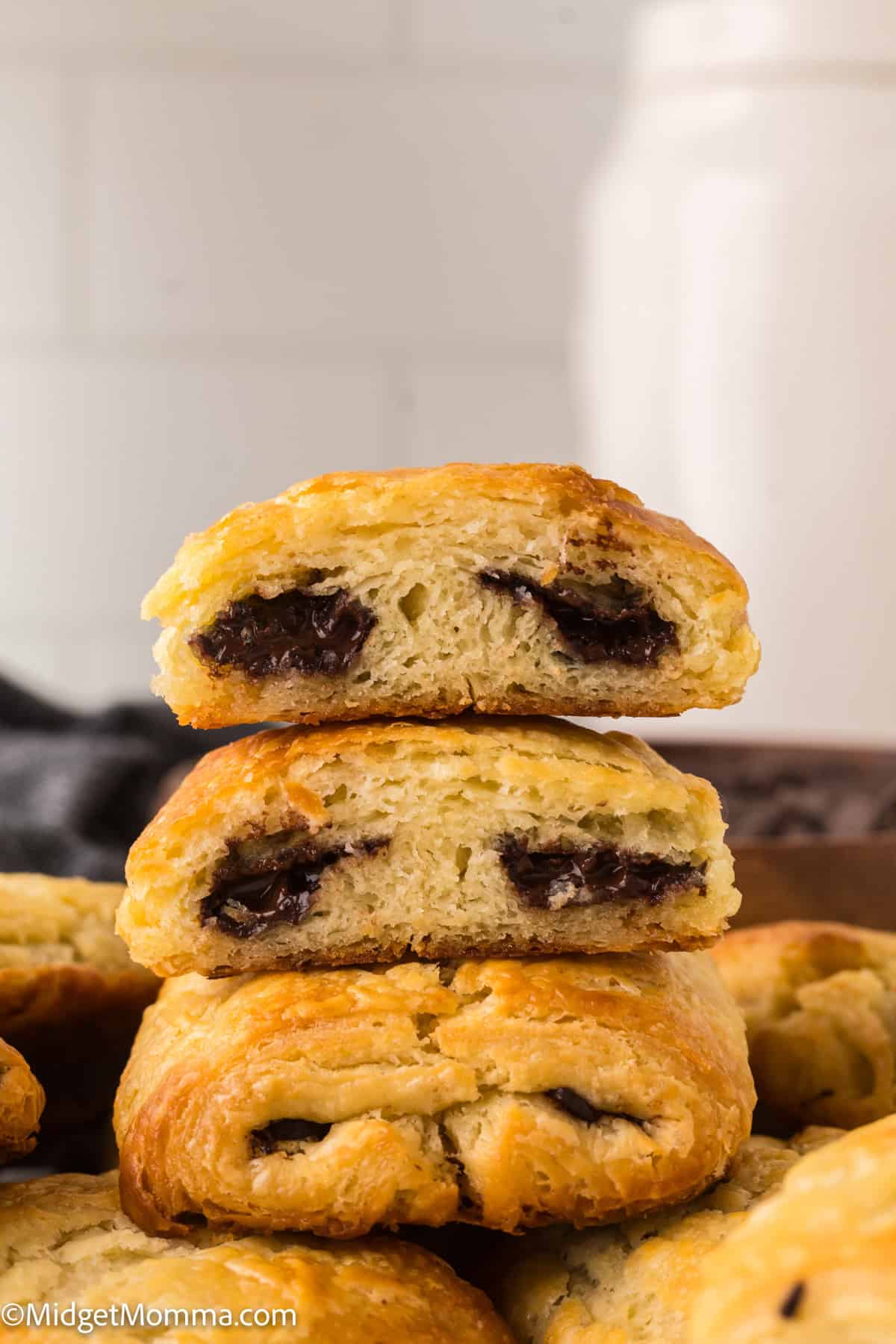 Two chocolate-filled pastries stacked with one cut open, revealing the chocolate inside. Other pastries are visible in the background.