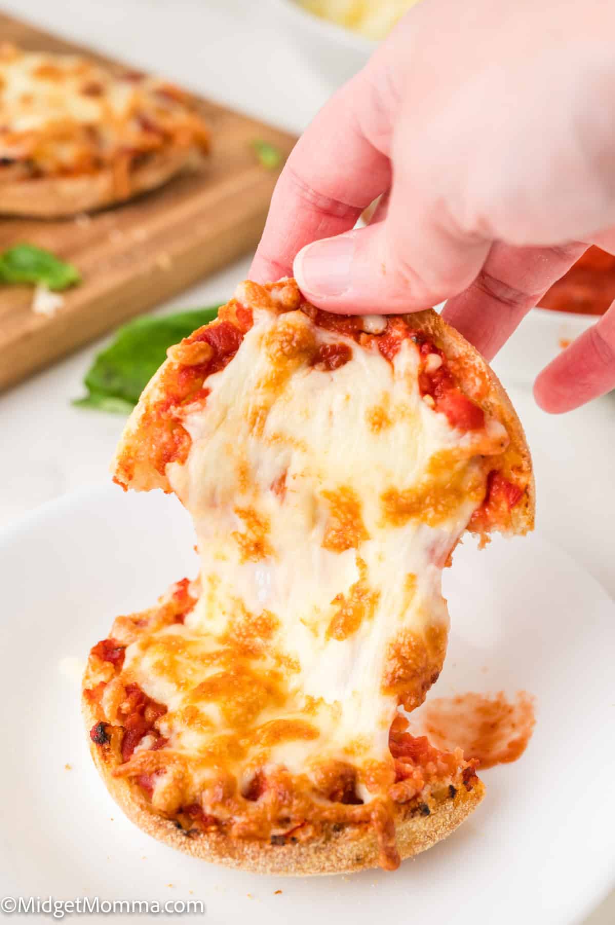 A hand pulling apart a mini pizza, revealing melted cheese and tomato sauce on a white plate.