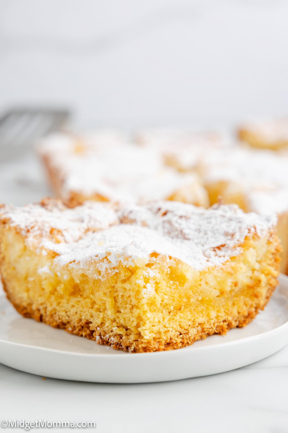 A slice of gooey butter cake dusted with powdered sugar on a white plate.