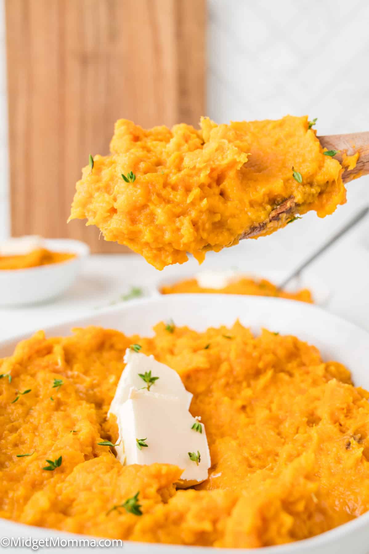 Spoonful of mashed sweet potatoes being served from a bowl, topped with a pat of butter and garnished with herbs.