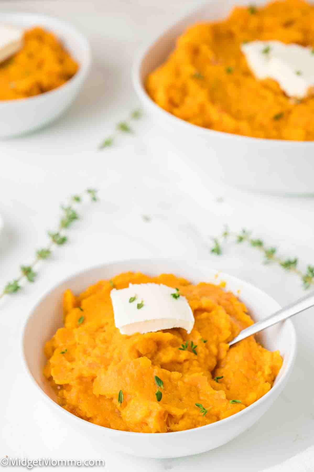 Bowls of mashed sweet potatoes topped with pats of butter, garnished with fresh thyme.