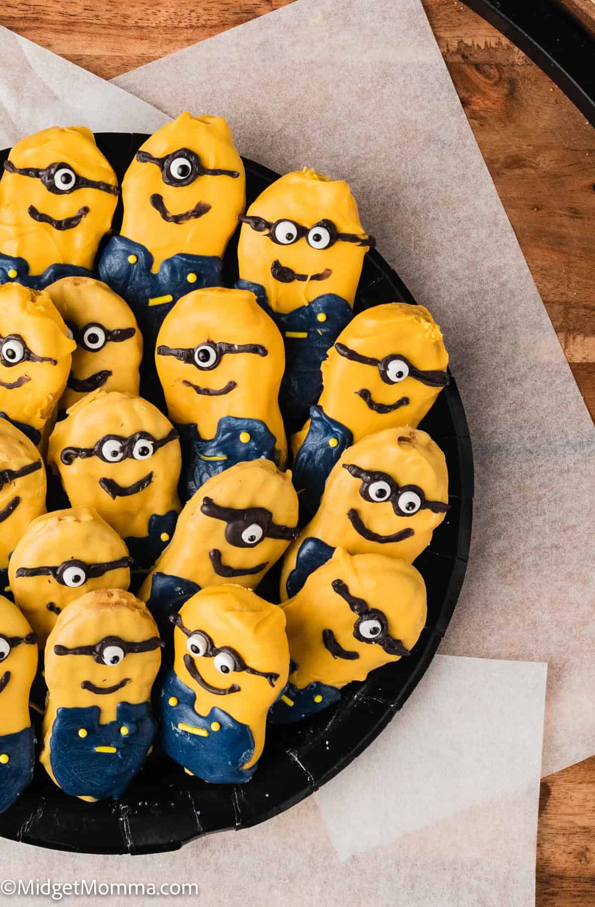 Cookies decorated to resemble yellow cartoon characters with blue overalls are arranged on a black plate.