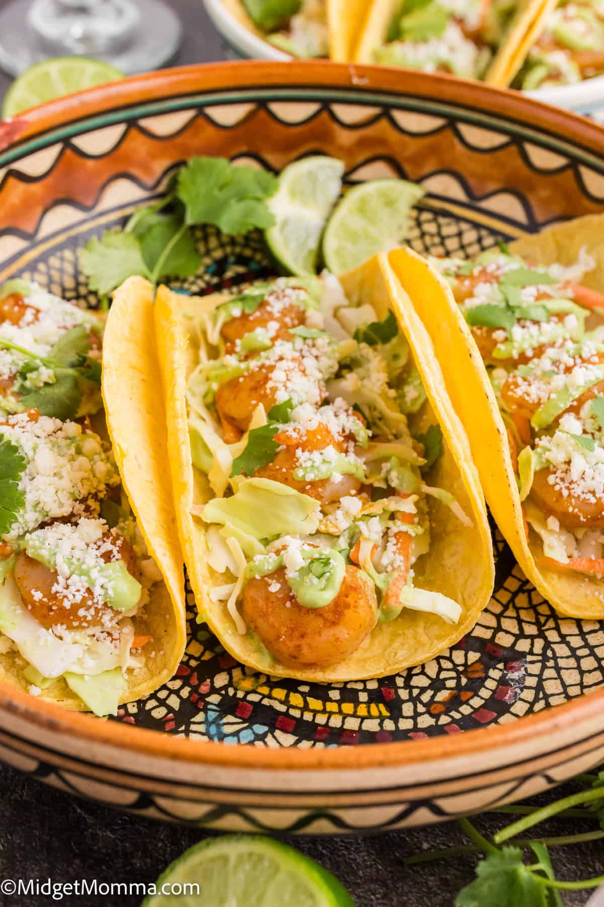 Three shrimp tacos with toppings, served in a decorative bowl, garnished with lime slices and cilantro.