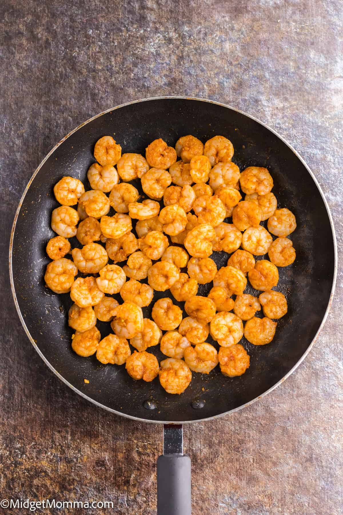 A frying pan filled with cooked shrimp on a textured surface.