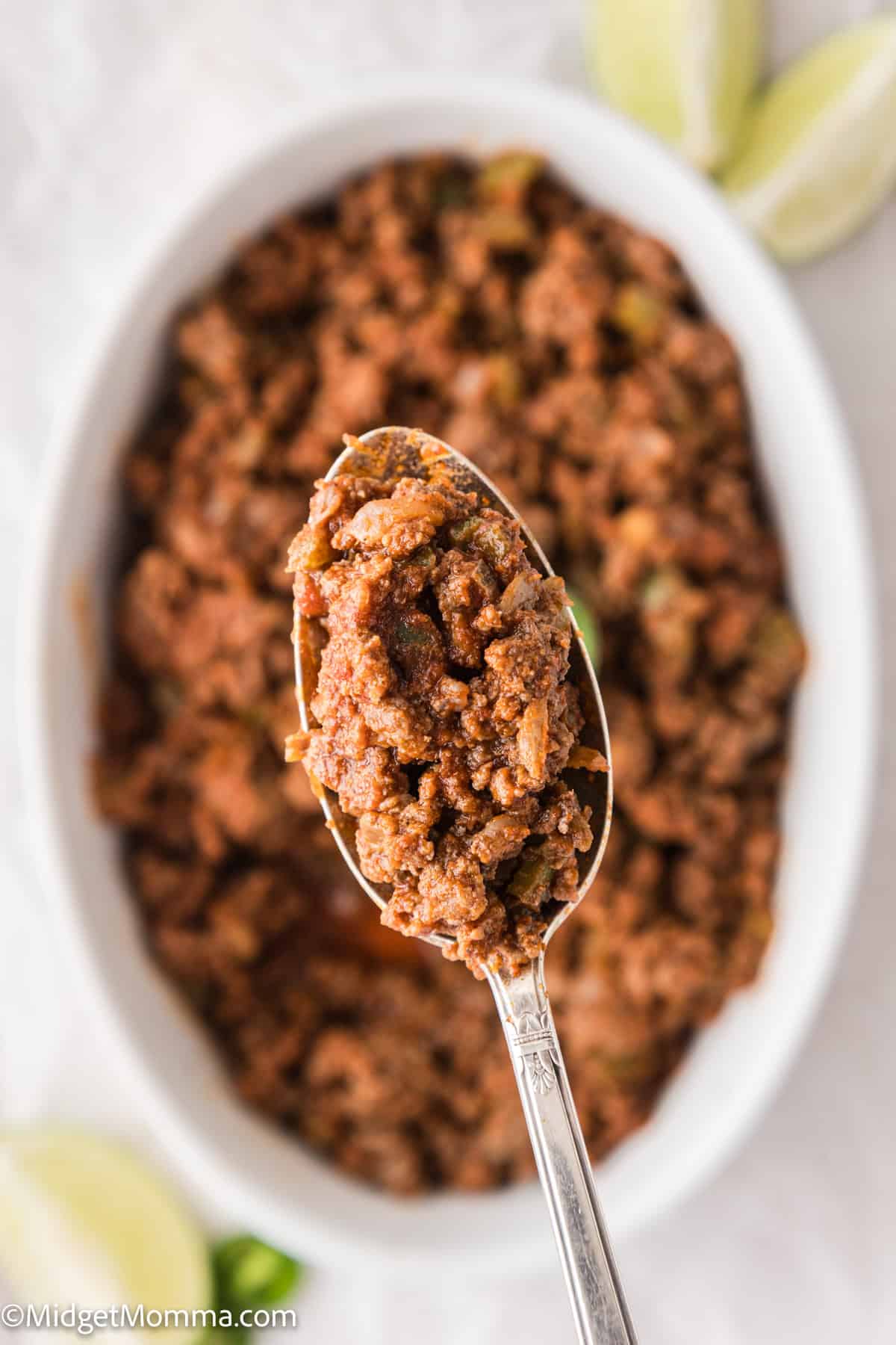 A spoonful of seasoned ground beef over a white oval dish with lime wedges in the background.