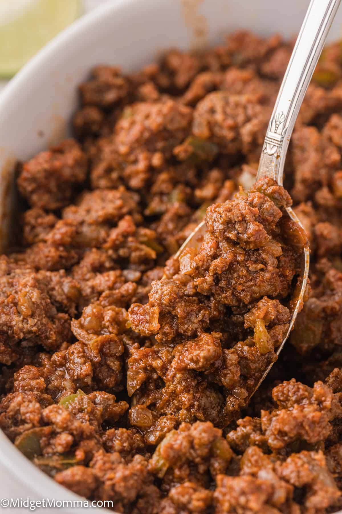 A bowl of cooked ground beef with visible seasonings and vegetables, served with a spoon.