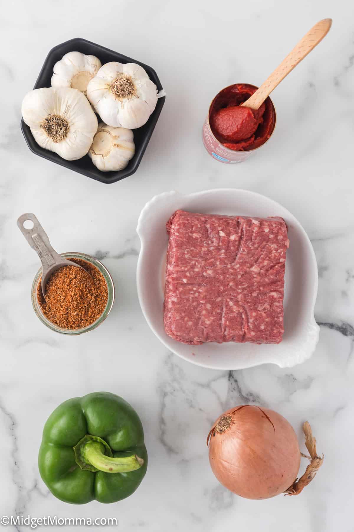 Stovetop Ground Beef Taco Meat Ingredients. Ground meat, green bell pepper, garlic, onion, tomato paste, and seasoning on a marble surface. 