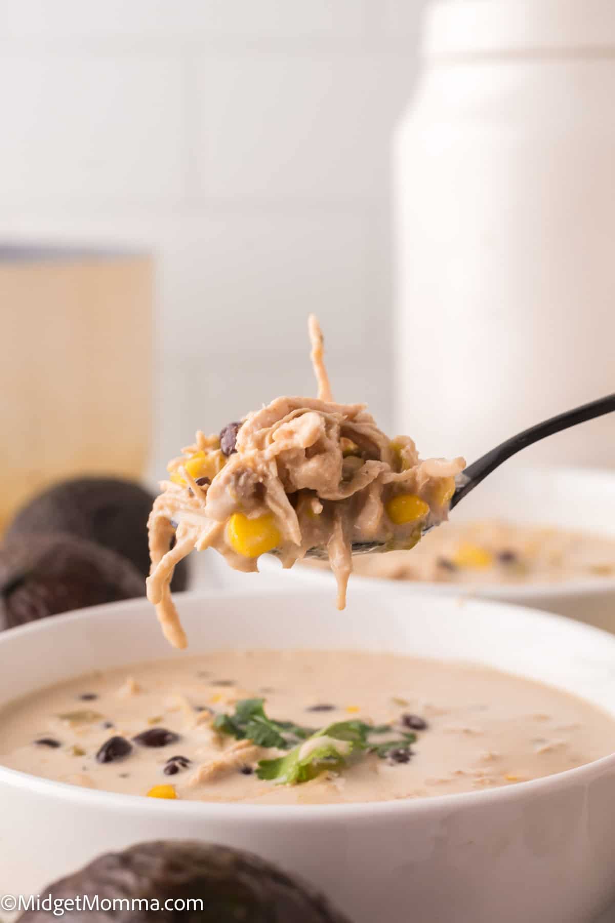 A spoonful of chicken chili over a bowl, showing shredded chicken, corn, and black beans.